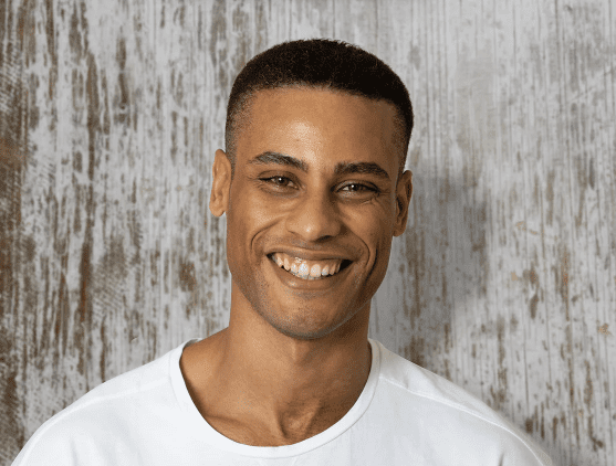 Smiling person wearing a white shirt against a textured, rustic wooden background. The mood is cheerful and relaxed.