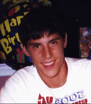 Smiling person wearing a white shirt with red and blue text. "Happy Birthday" balloon in the colorful background, festive mood.