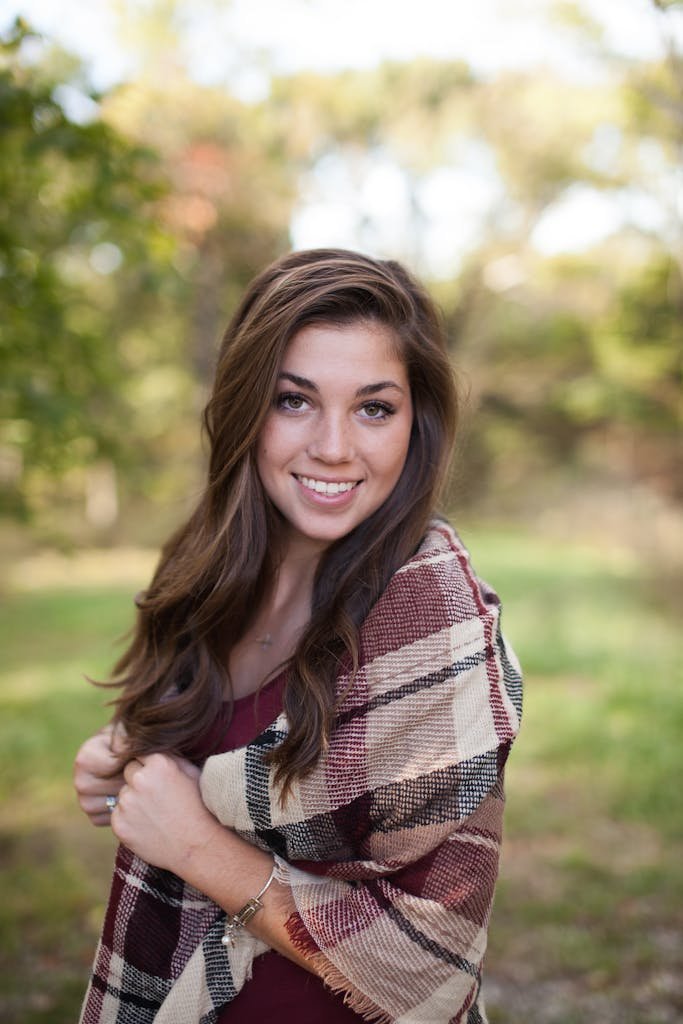 Porcelain Veneer Costs: The Real Price, Lifetime Expenses, and Safer Alternatives 8 A woman smiling outdoors with a cozy plaid shawl, surrounded by nature in a sunny park.
