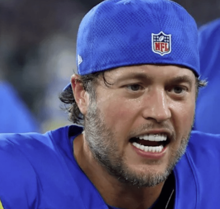 Matthew Stafford Veneers Before and After: Who’s Really to Blame? 6 Matthew Stafford wearing a blue Rams cap and uniform, showing his fake white porcelain veneers while speaking on the sidelines.