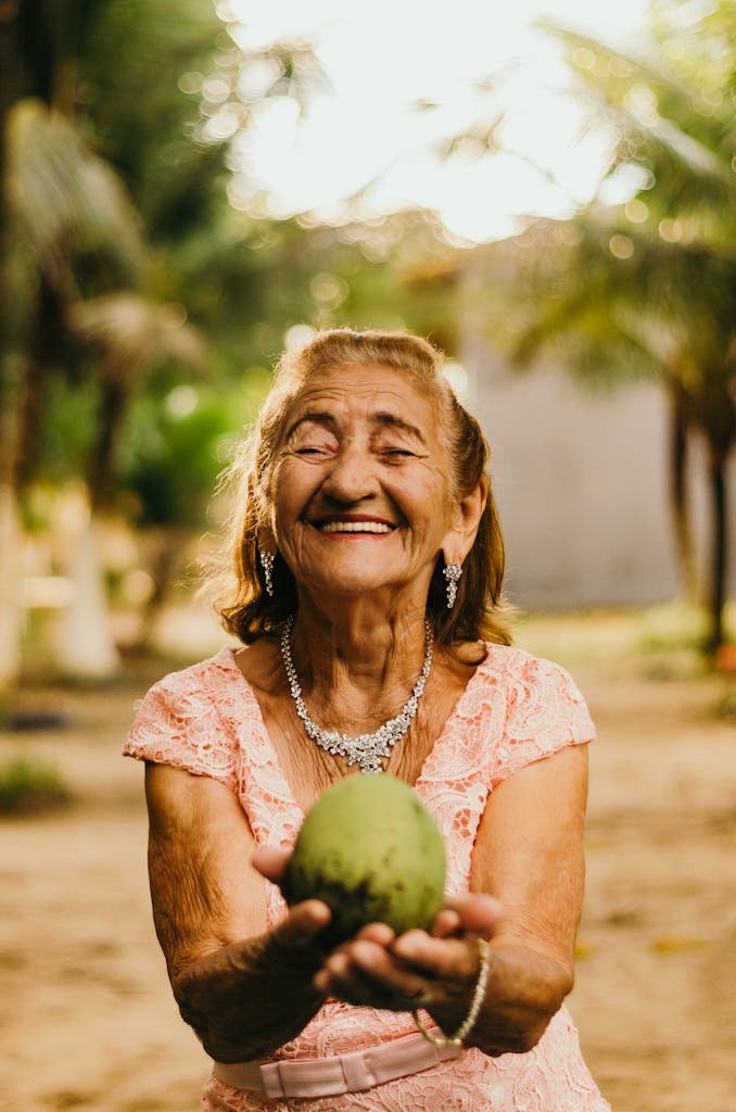 Porcelain Veneer Costs: The Real Price, Lifetime Expenses, and Safer Alternatives 4 Smiling elderly woman with jewelry showcases happiness while holding a mango outdoors.