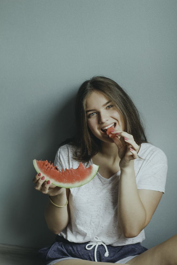 Why So Many People Regret Veneers and What You Should Know First 6 Smiling young woman sitting indoors enjoying a fresh slice of watermelon.